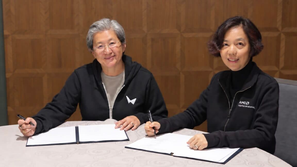 Deux femmes en sweat à capuche noir sourient face à l'objectif, assises à un bureau couvert de documents à signer : l'une d'AMD porte un sweat World Labs, l'autre de World Labs porte un sweat AMD.